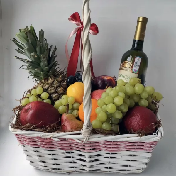 Плетёная корзина с ананасом, виноградом, яблоками, грушами и бутылкой вина