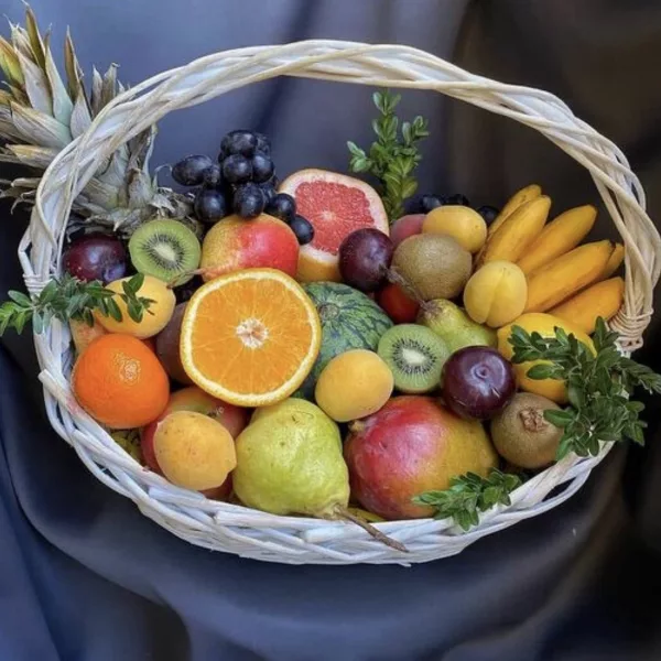 Плетёная светлая корзина с ананасом, апельсинами, киви, манго, виноградом и бананами
