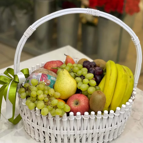 Белая плетёная корзина с виноградом, грушами, яблоками, бананами и киви, зелёный бант
