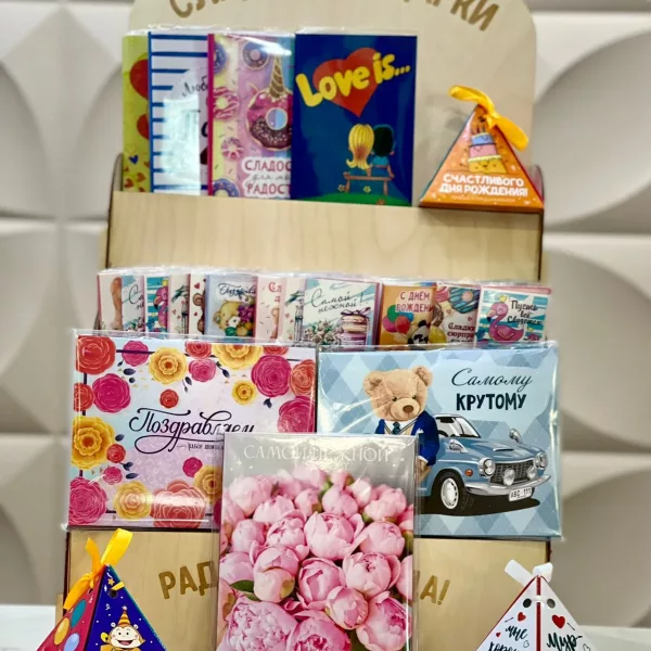 Подарочный набор с открытками, розовыми бумажными цветами и шоколадными конфетами на деревянной полке