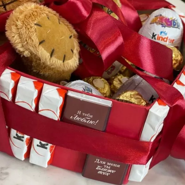Деталь композиции: плюшевый медведь, конфеты Kinder и Ferrero Rocher в красной картонной коробке с белыми полосами