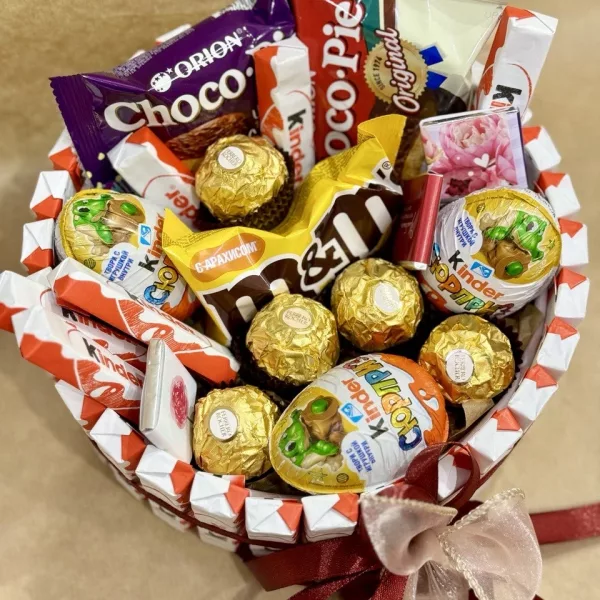 Корзина с золотистыми конфетами Ferrero Rocher, шоколадом Kinder и сладостями на белой клетчатой ткани с бордовым бантом