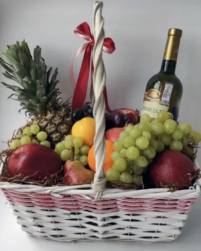 Плетёная корзина с ананасом, виноградом, яблоками, грушами и бутылкой вина