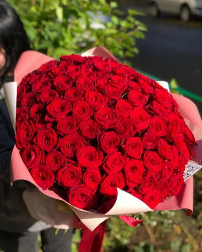 Крупный план букета из алых роз с белым подкладом в розовой упаковочной бумаге