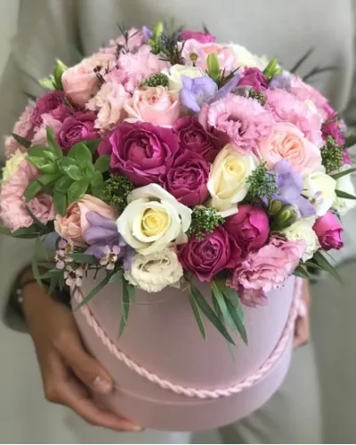 Шляпная коробка розового цвета с куполом из малиновых кустовых роз, кремовых роз, розовых эустом и сиреневой фрезии