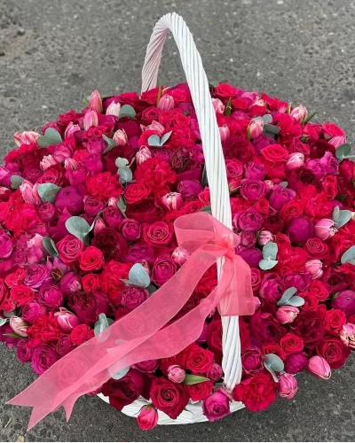 Большая белая плетёная корзина с малиновыми пионами, красными розами и розовыми тюльпанами, розовая лента