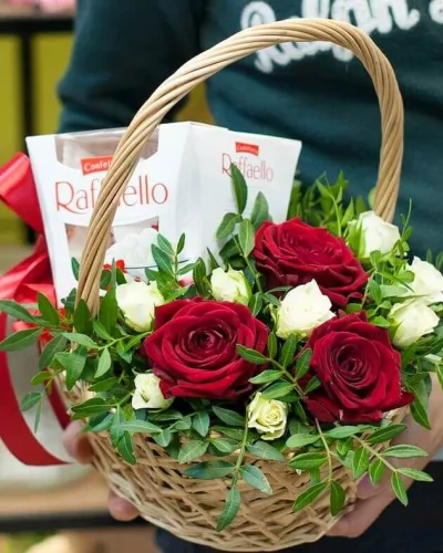Плетёная корзина с красными розами, белой кустовой розой, писташем и Raffaello