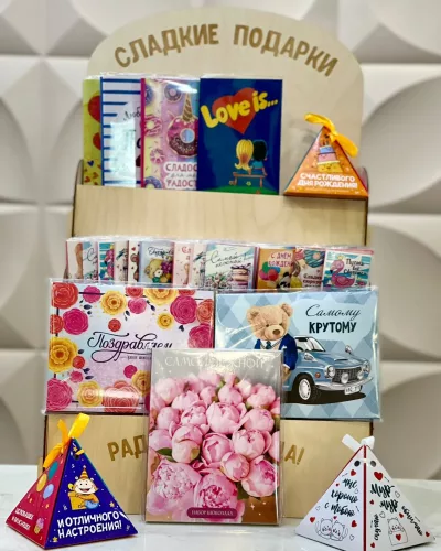 Подарочный набор с открытками, розовыми бумажными цветами и шоколадными конфетами на деревянной полке