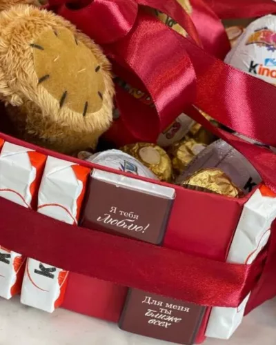 Деталь композиции: плюшевый медведь, конфеты Kinder и Ferrero Rocher в красной картонной коробке с белыми полосами