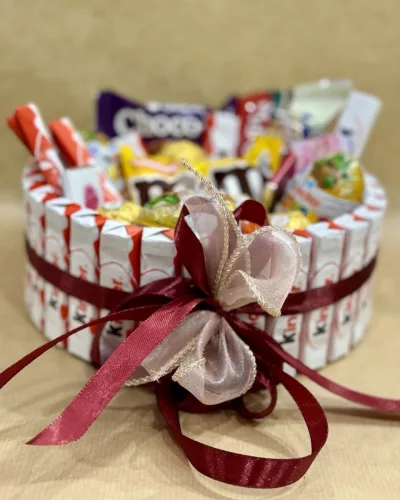 Корзина со сладостями Kinder и Ferrero Rocher, украшена бордовыми лентами и розовым бантом
