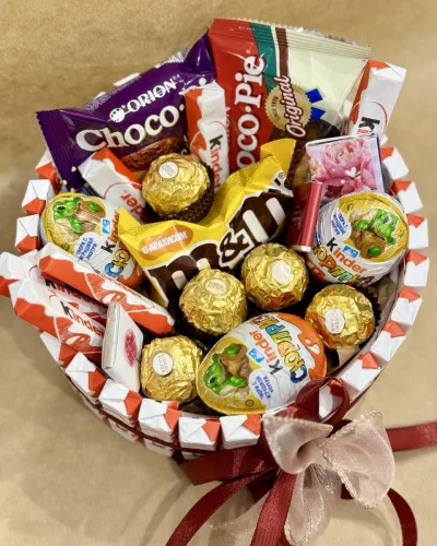 Корзина с золотистыми конфетами Ferrero Rocher, шоколадом Kinder и сладостями на белой клетчатой ткани с бордовым бантом